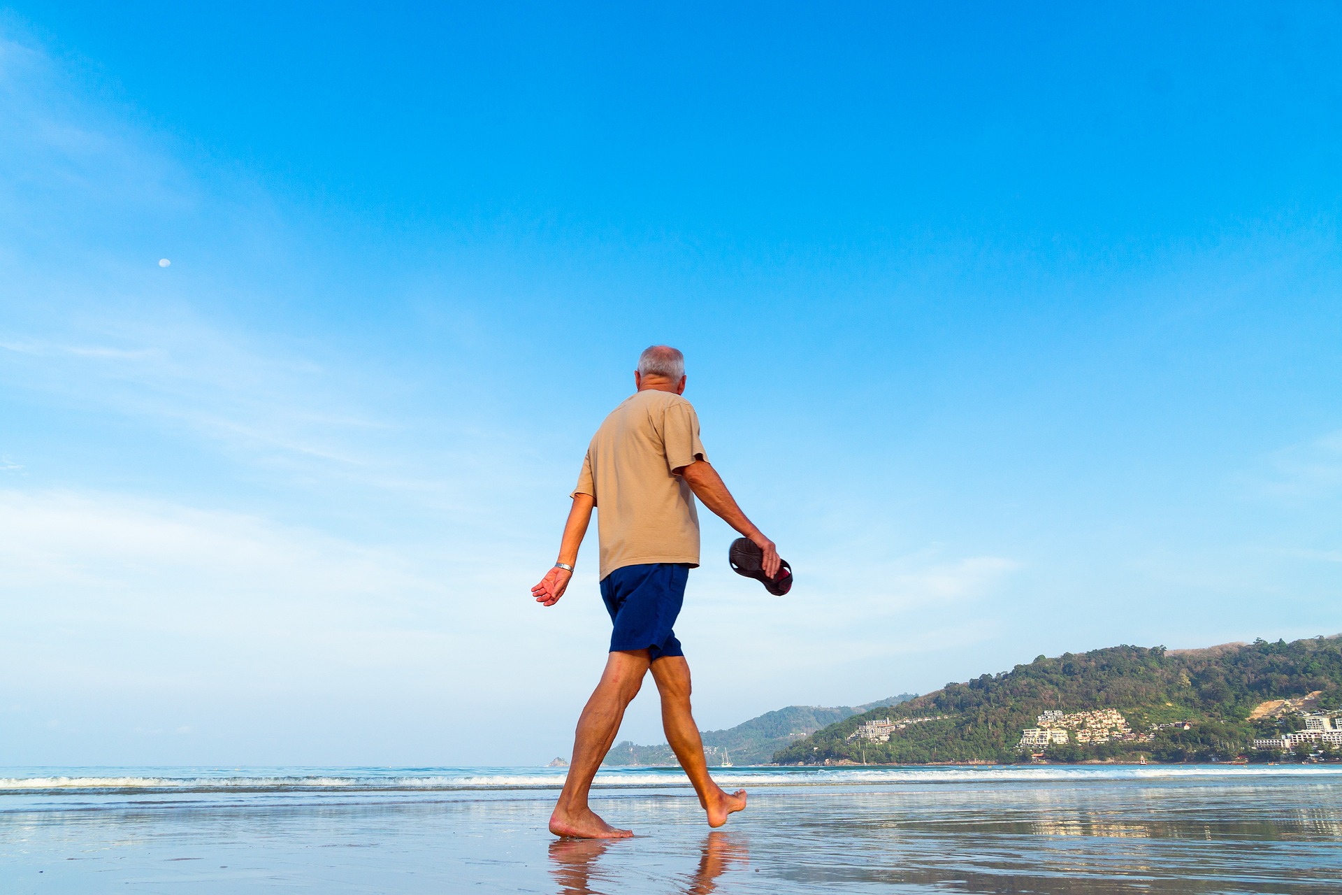 Senior investor walking along the Belize shoreline reflecting on retirement investment goals